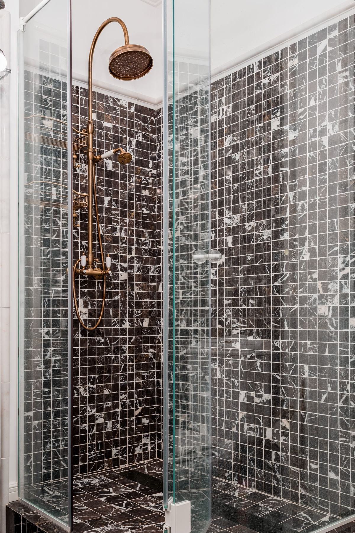 A walk-in shower with brass fittings and mosaic tiles